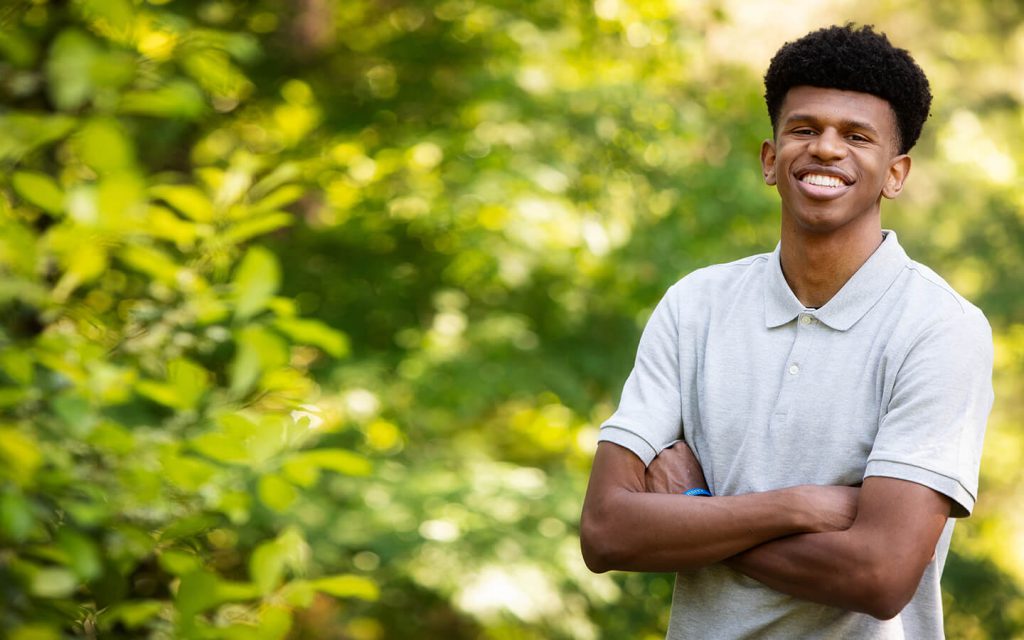 African American teen wearing a light gray shirt, in a natural setting.