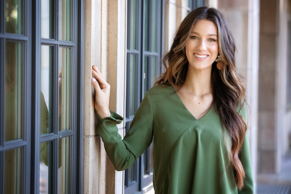 Brunette with long hair, wearing a green blouse and smiling