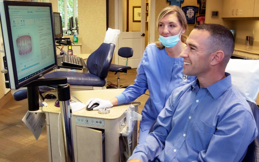 an assistant and a male patient looking at the digital impressions of his bite in a dental office