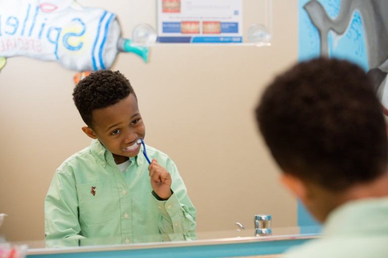 young boy looking at himself in the mirror while brushing his teeth